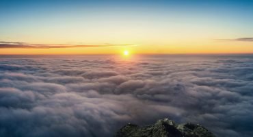 Photographer hand holding camera and standing on viewpoint over clouds. Panorama viewpoint at sunrise.